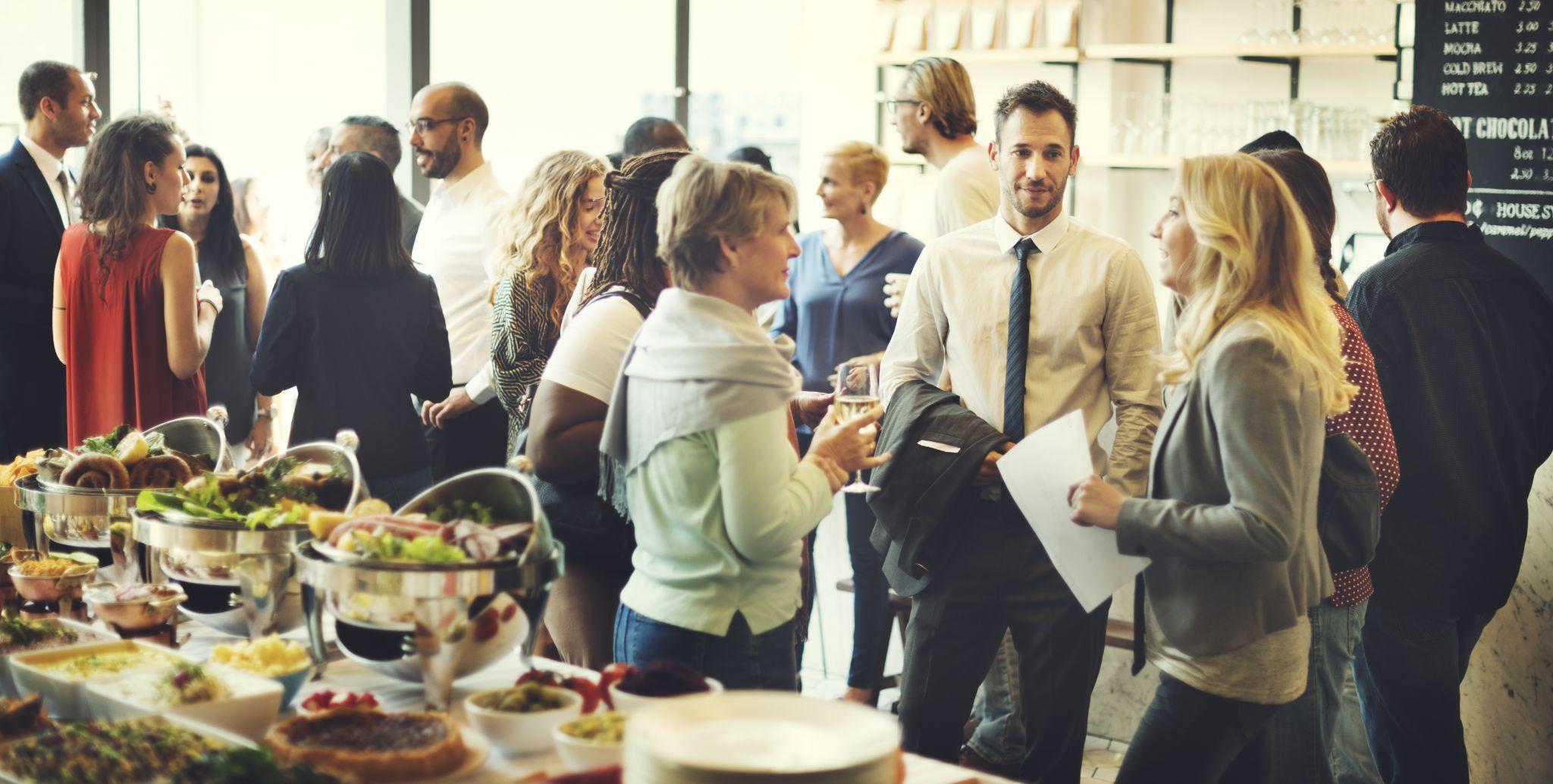 Professionals mingling and networking beside a buffet table at a business event during the day.